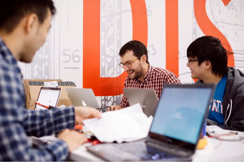 Three people are working together on laptops in an office setting.