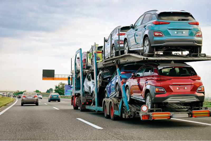 A truck transports new cars on a highway under a cloudy sky.