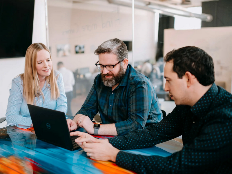 Three people collaborating while looking at a laptop in a modern office setting.