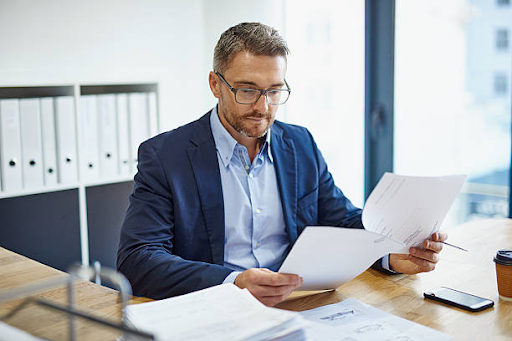 A businessman reviews documents at a desk, focusing on license costs in the RAK Free Zone for various businesses.